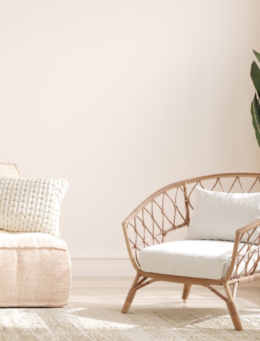 Décoration Salon Bohème Chic : Fauteuil Rotin et Coussins Coin salon lumineux avec fauteuil en rotin tissé, coussins blancs texturés, mur beige clair, et tapis texturé au sol.